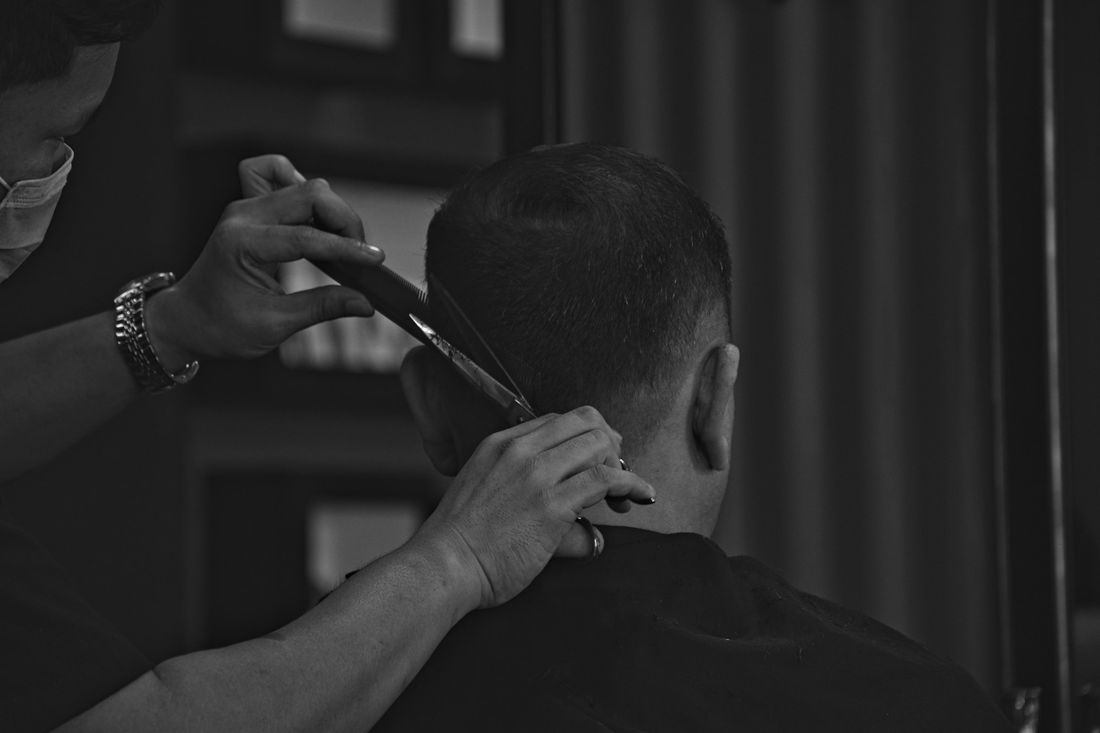 A barber working on the back of a client's head in a dim shop