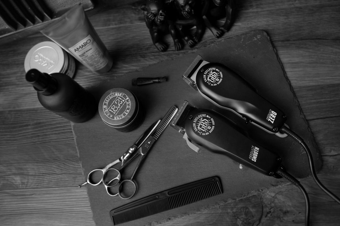 Two pairs of hair clippers, scissors, a comb and grooming products laid out on a slate board