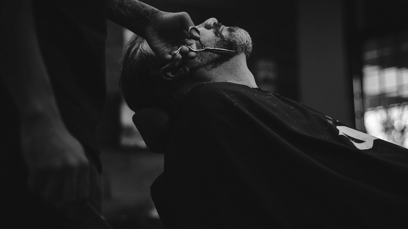 A man leaning back in a leather barber chair under warm shop lights
