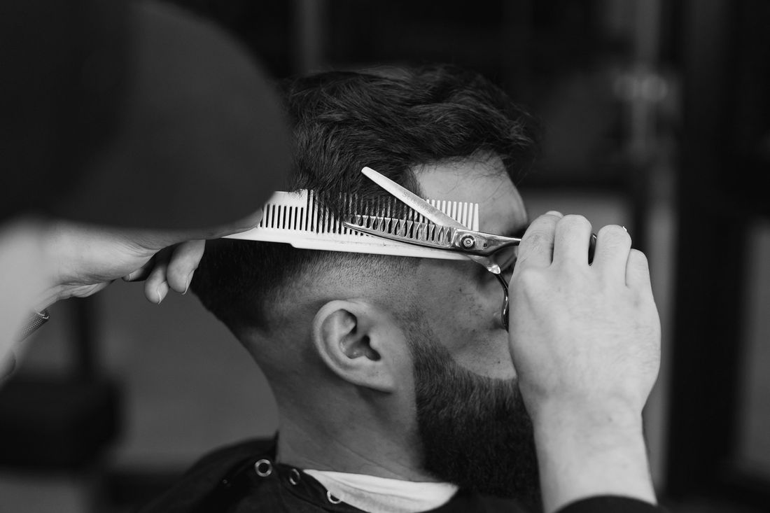 A barber cutting a client's hair with scissors and a comb