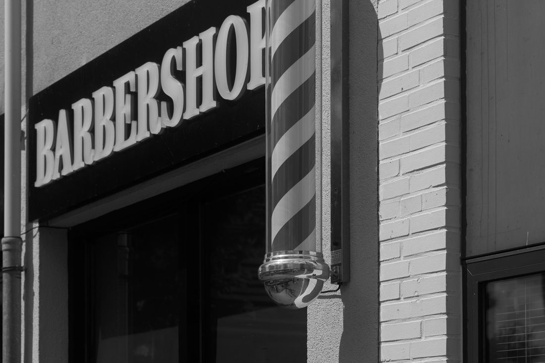 A barbershop storefront sign beside a traditional striped barber pole
