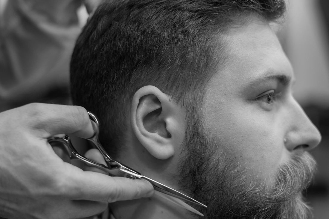 A barber trimming a client's beard with scissors and a comb