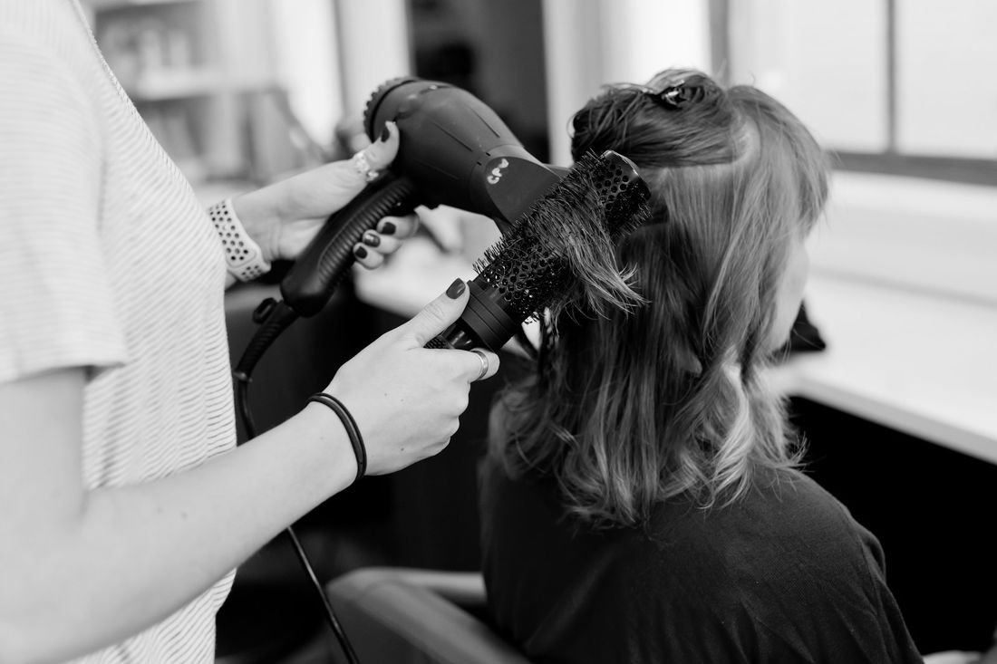 A hairstylist blow-drying a client's long hair with a round brush