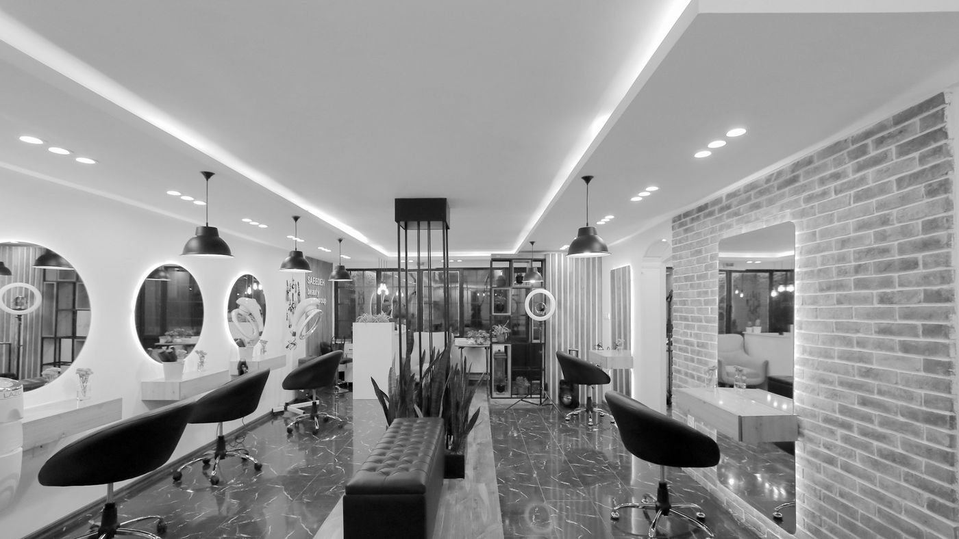 A bright modern salon with black chairs, round mirrors and a brick wall
