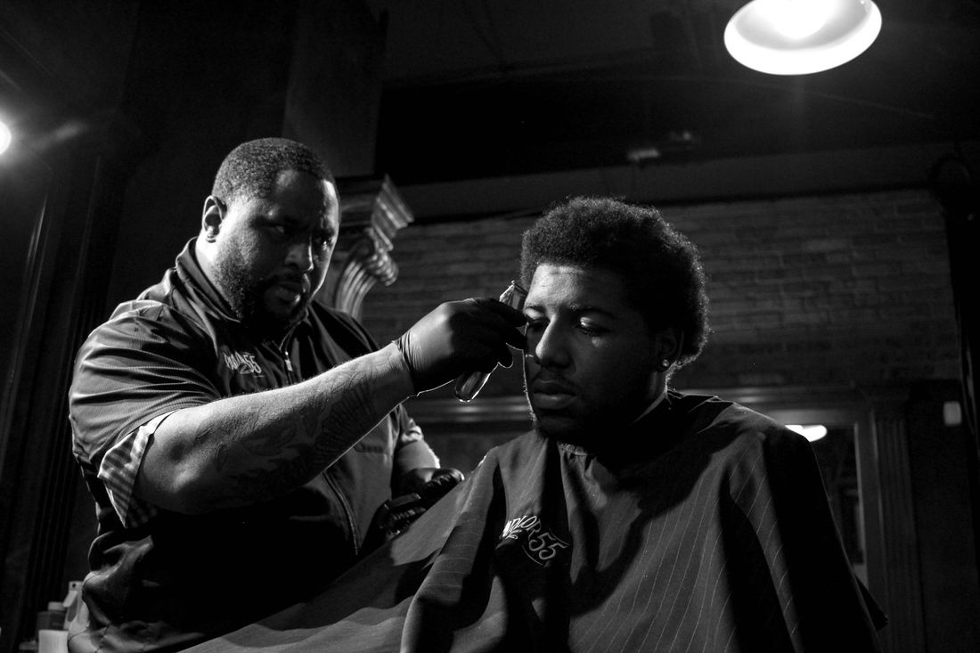 A barber cutting a young man's hair in a dimly lit shop