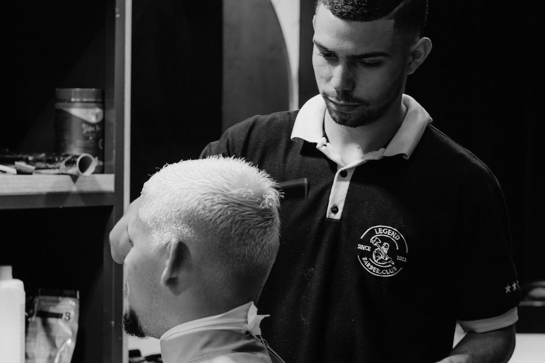 A barber in a polo shirt cutting a light-haired client's hair