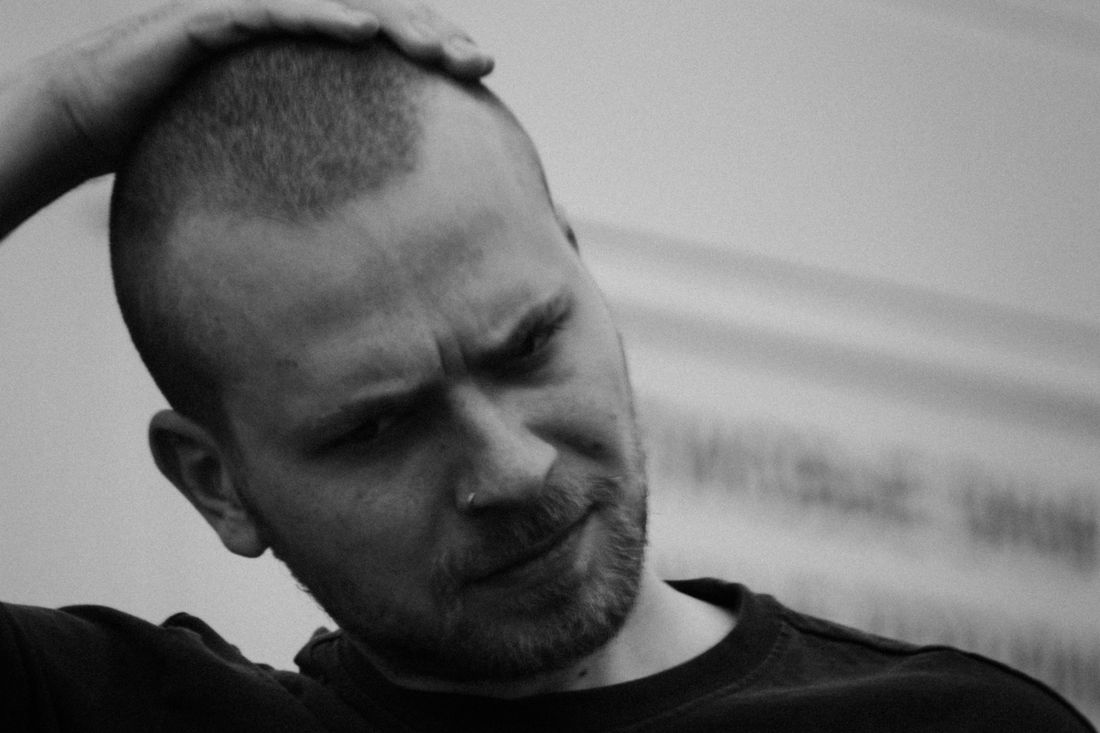 A man with short hair and a beard resting a hand on his head