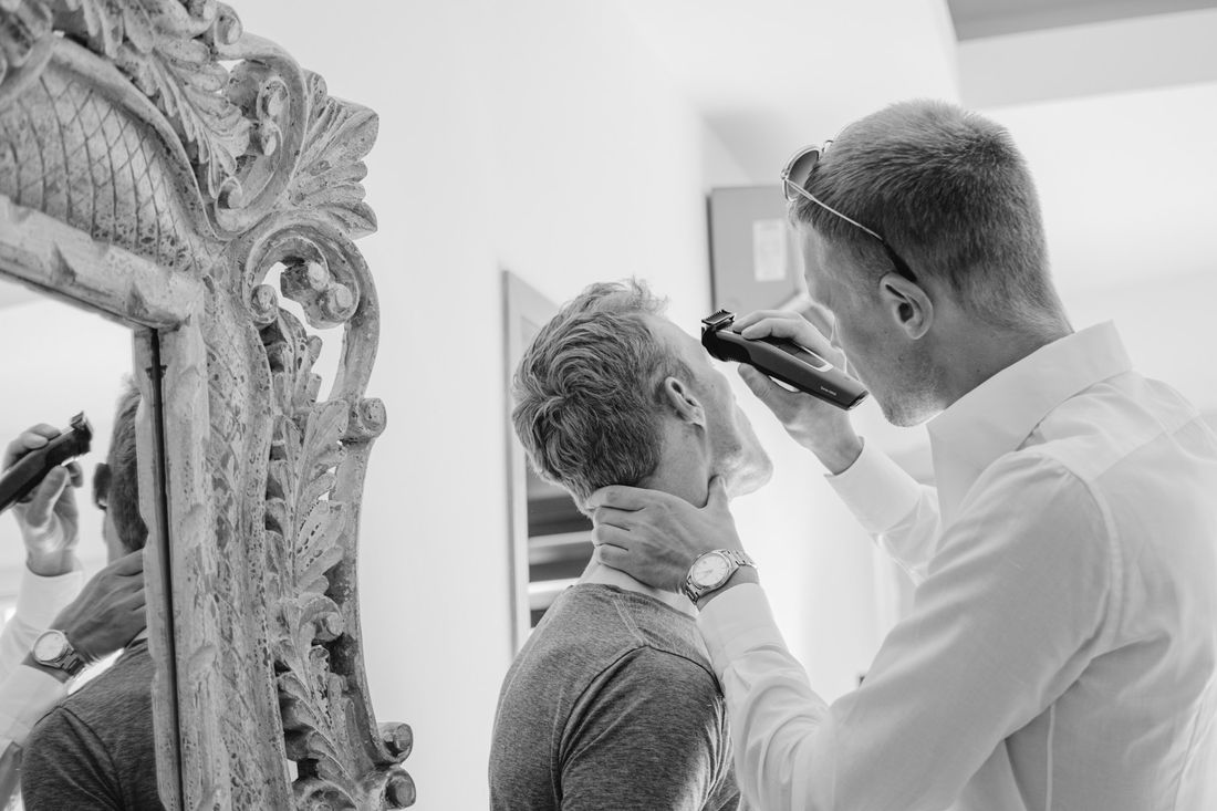 A barber trimming a client's neckline in front of an ornate mirror