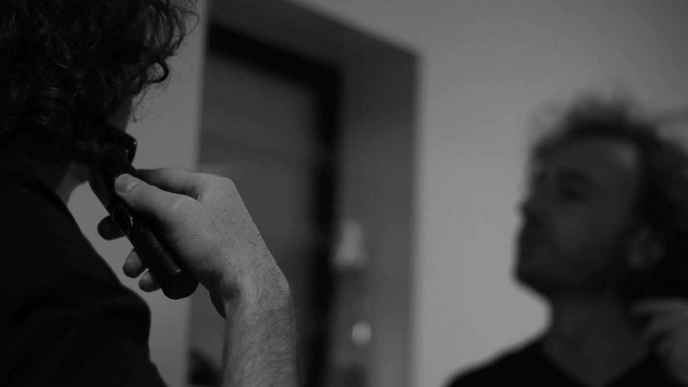 A man trimming the beard line on his neck in a mirror