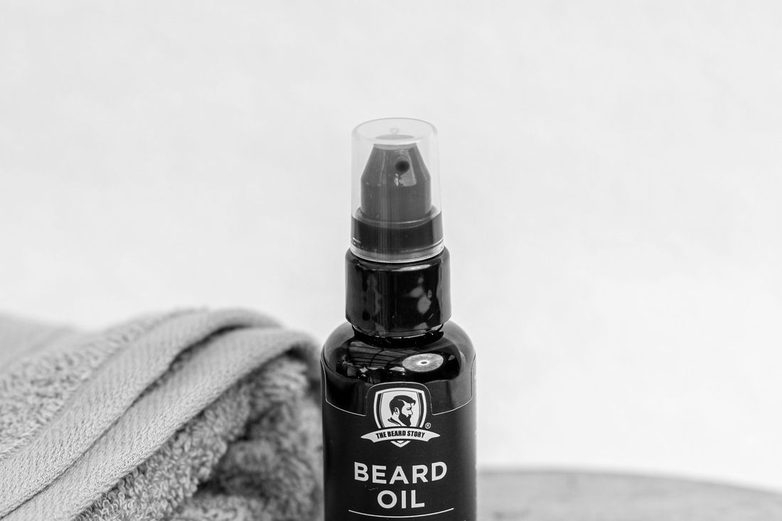 A small dropper bottle of beard oil next to a folded towel