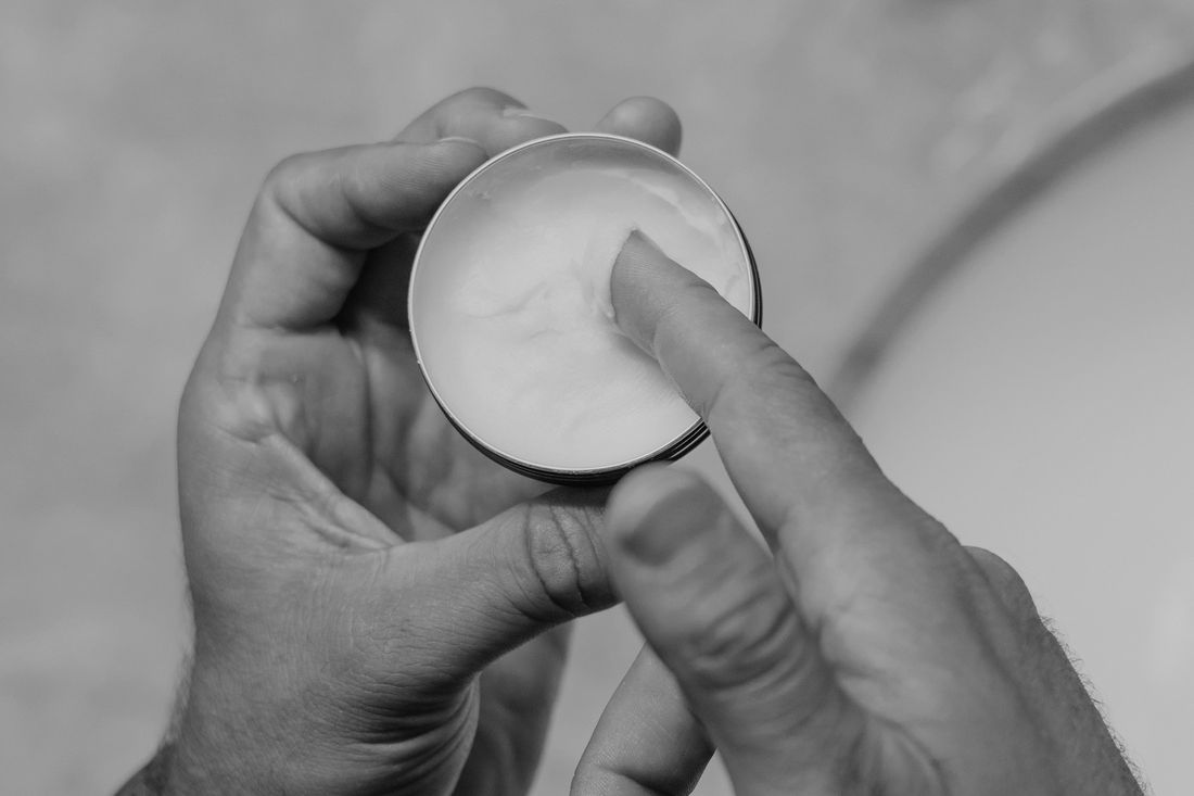 Hands holding an open tin of balm