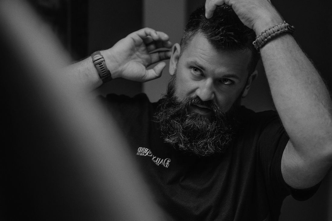 A bearded man working his fingers through his hair in a mirror