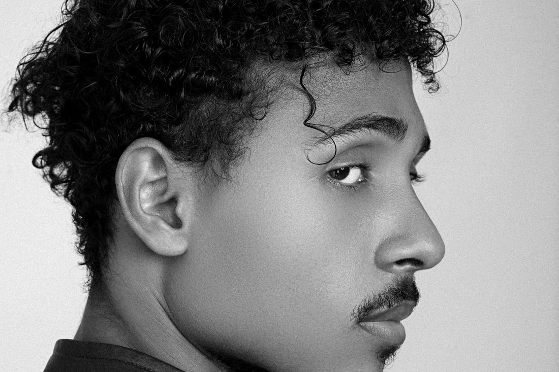 Profile of a young man with curly hair, a mustache and chin hair