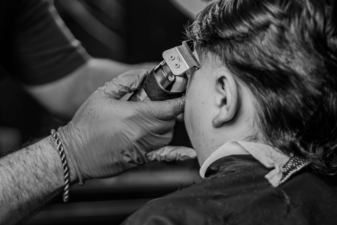 A gloved barber running clippers up the back of a client's curly hair