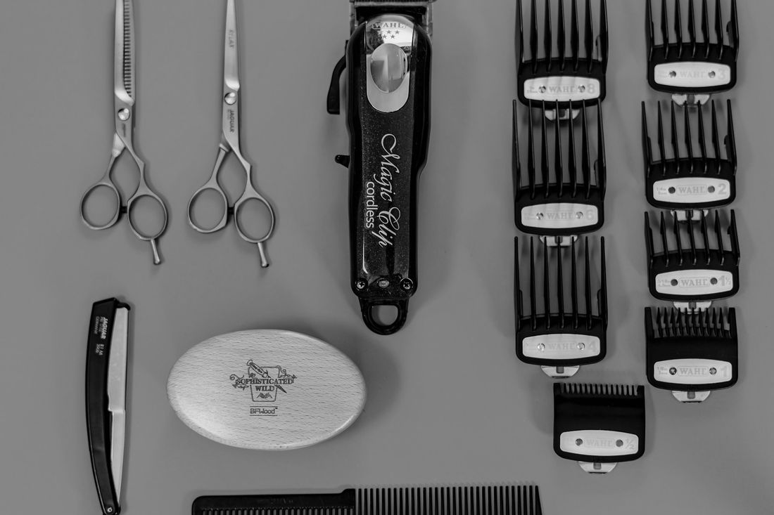 A flat lay of a hair clipper, a set of clipper guards, scissors and a straight razor