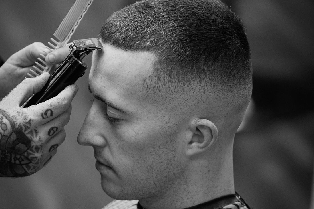 A barber running a clipper along the temple of a man with a short fade