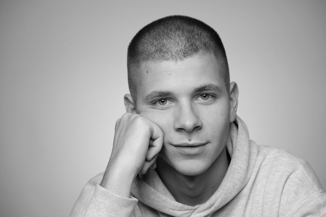 A smiling man with a short buzz cut resting his chin on his hand