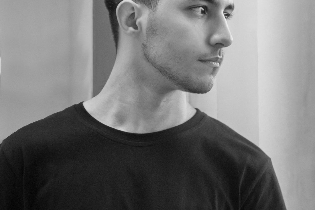 A young man with short, neat hair in profile wearing a black T-shirt