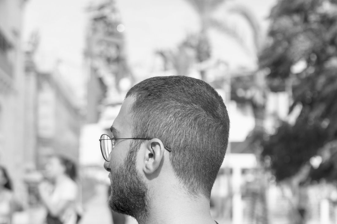 A man with a short buzz cut and glasses seen in profile outdoors