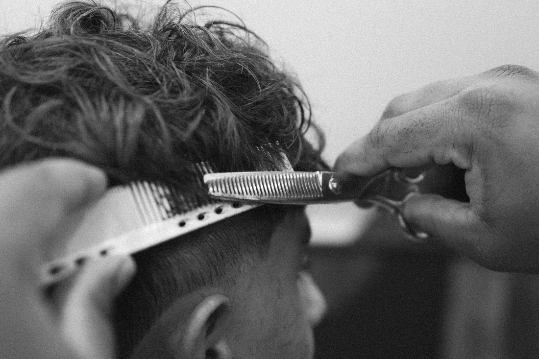 A barber cutting along a comb through a client's wavy hair