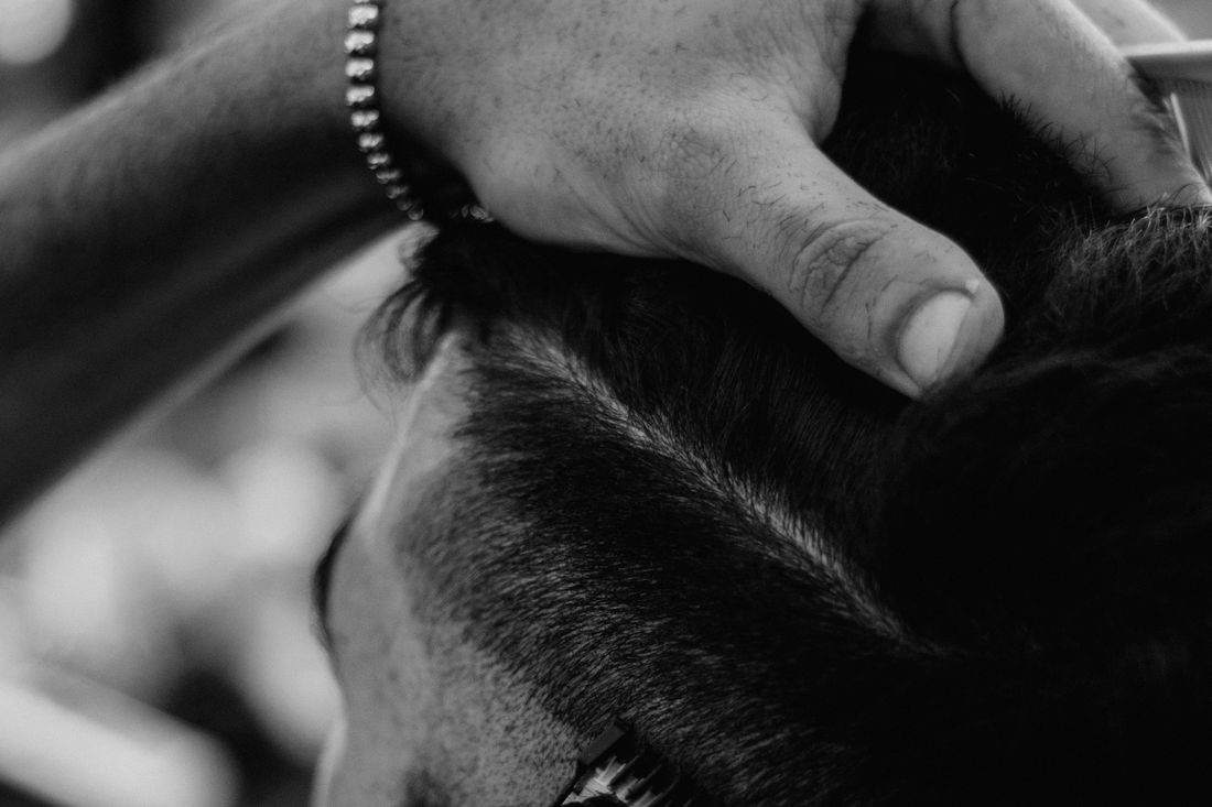 Close-up of a barber's hands holding a client's head while cleaning the hair at the temple