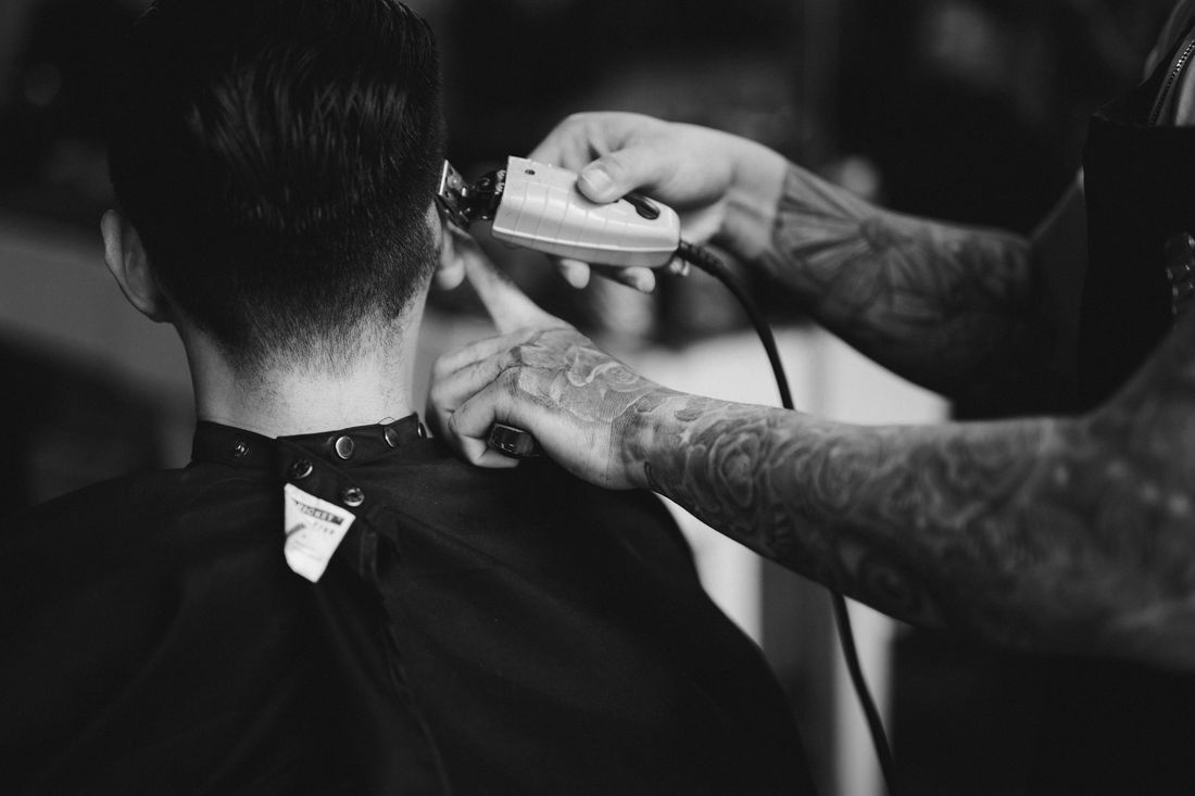 A barber using white clippers along the back of a client's neck