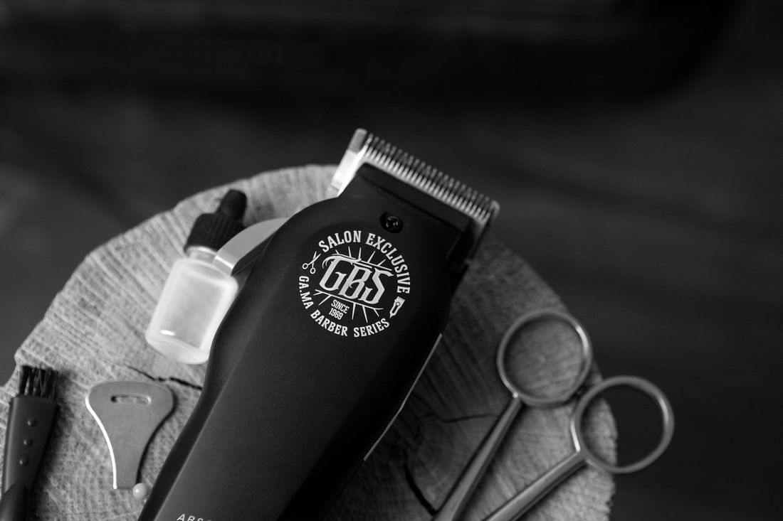 A cordless clipper and barber scissors on a dark surface