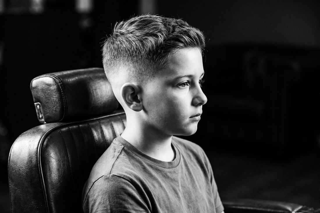 A boy with a mid fade haircut, the blend starting around the temple, halfway up the side of the head