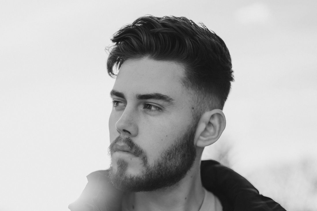 A young man with a short haircut and beard looking to the side
