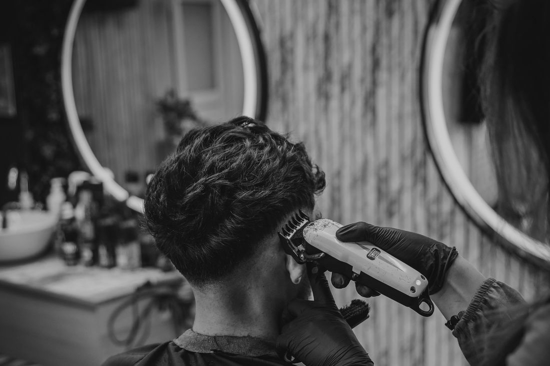 A barber running clippers over a client's curly hair in front of a round mirror