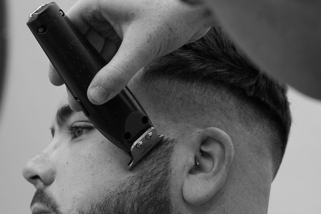 A barber's clipper working up the side of a young man's head
