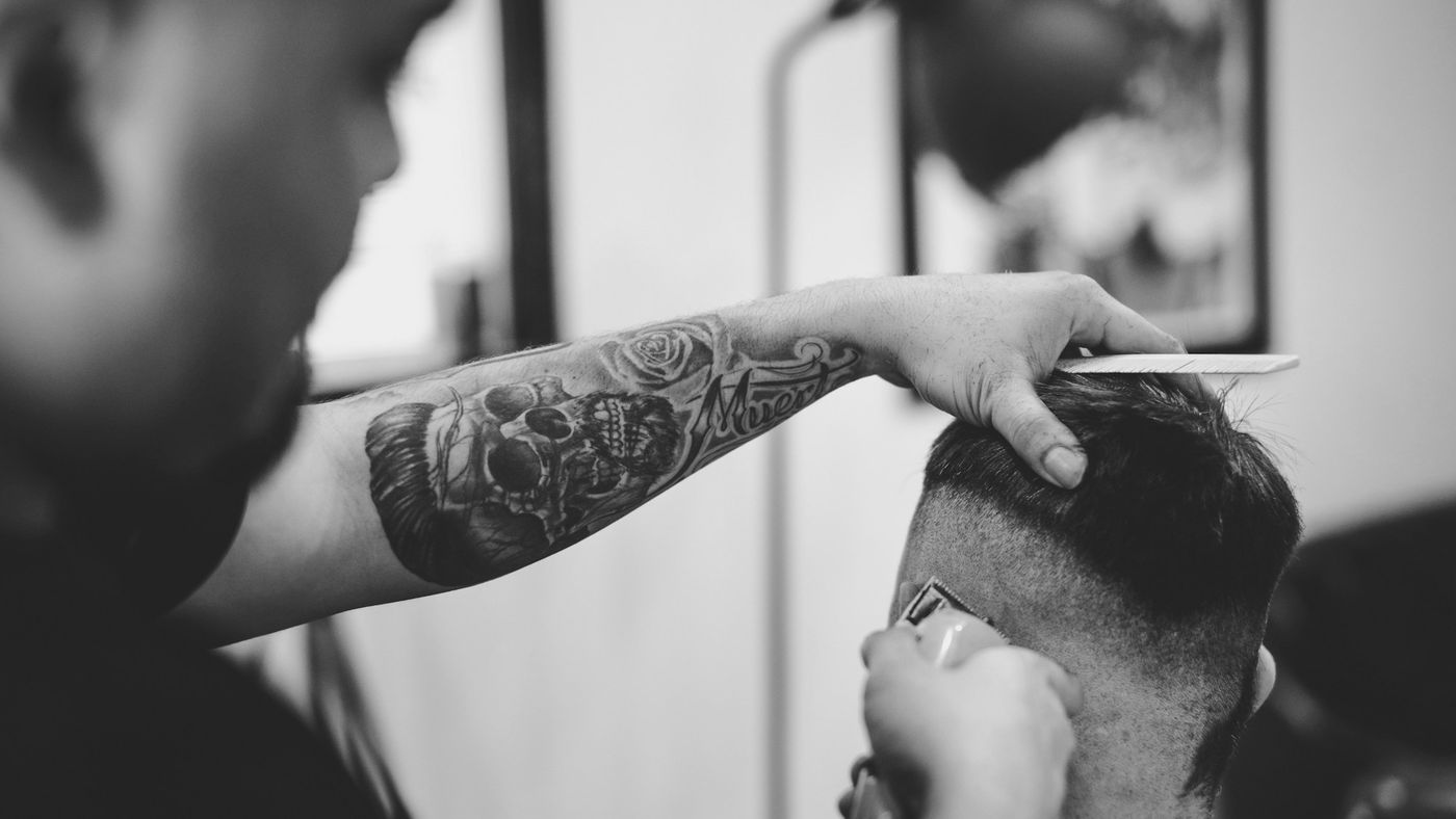 A tattooed barber shaping the side of a client's haircut