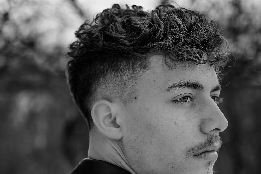 A young man with a curly textured top and a sharp skin fade