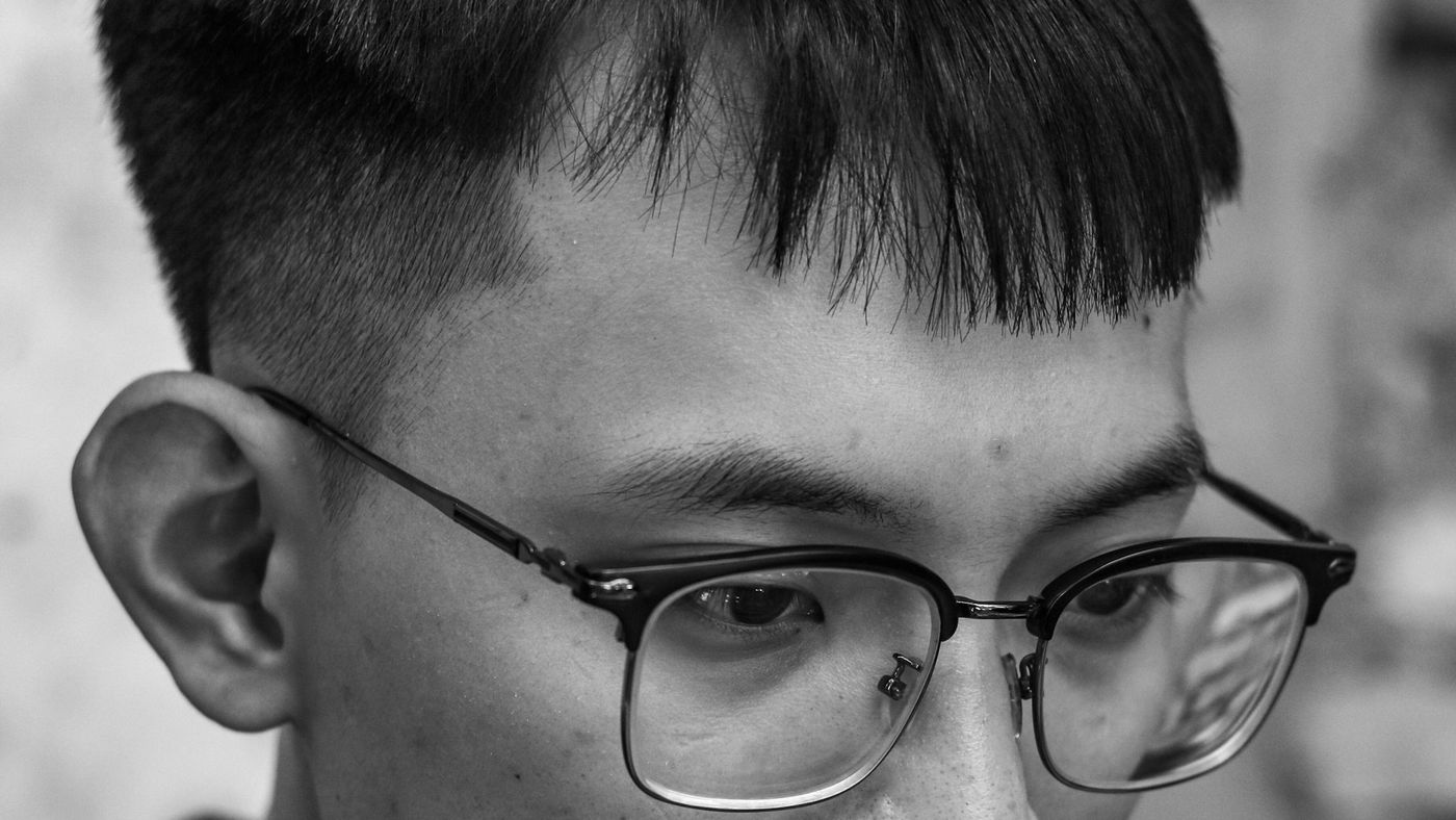 A young man in glasses with short, blunt bangs and faded sides