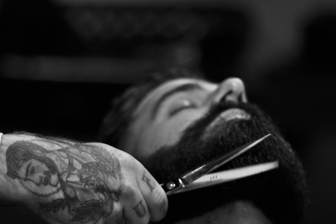 A barber trimming the edge of a client's beard with scissors