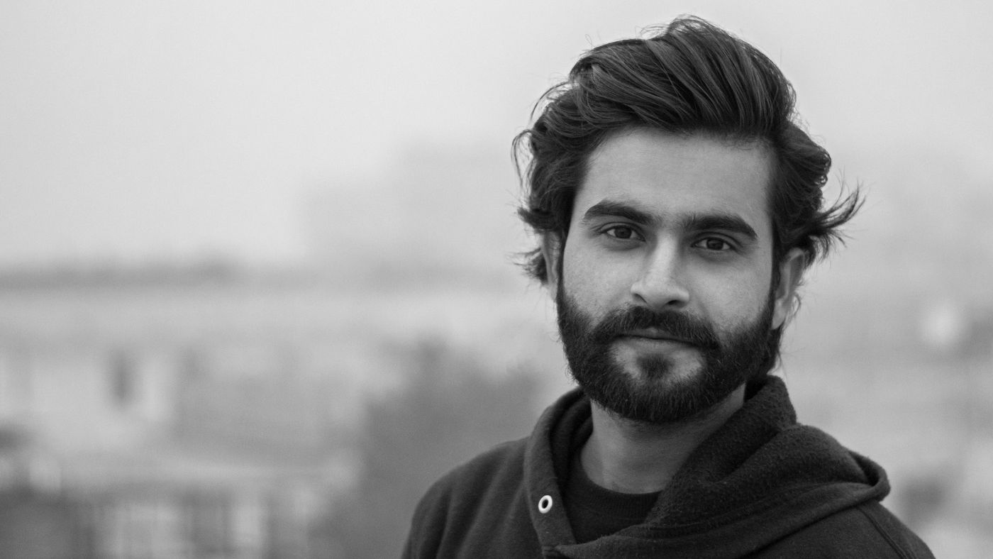 A man with a full, neatly kept beard looking at the camera outdoors