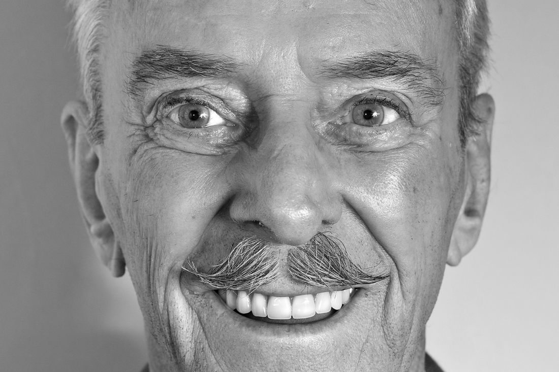 An older man with a gray mustache smiling broadly