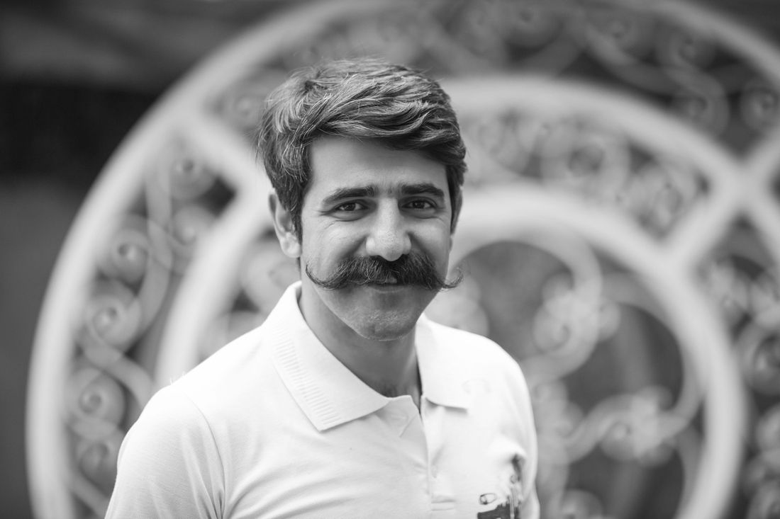 A man with curly hair and a mustache in a white polo shirt