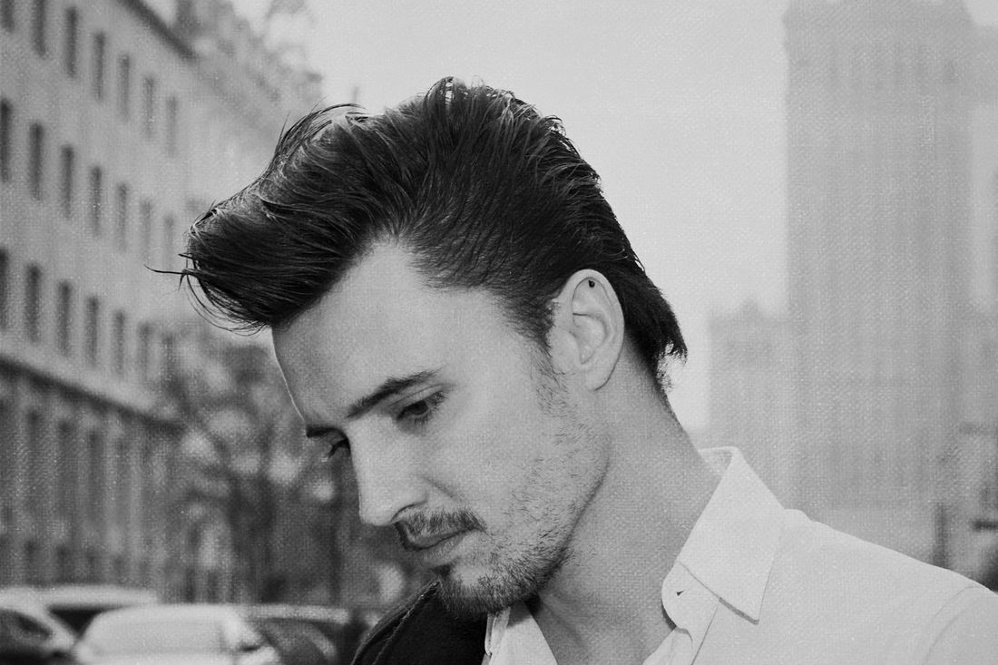 A man with medium-length hair swept back, on a city street