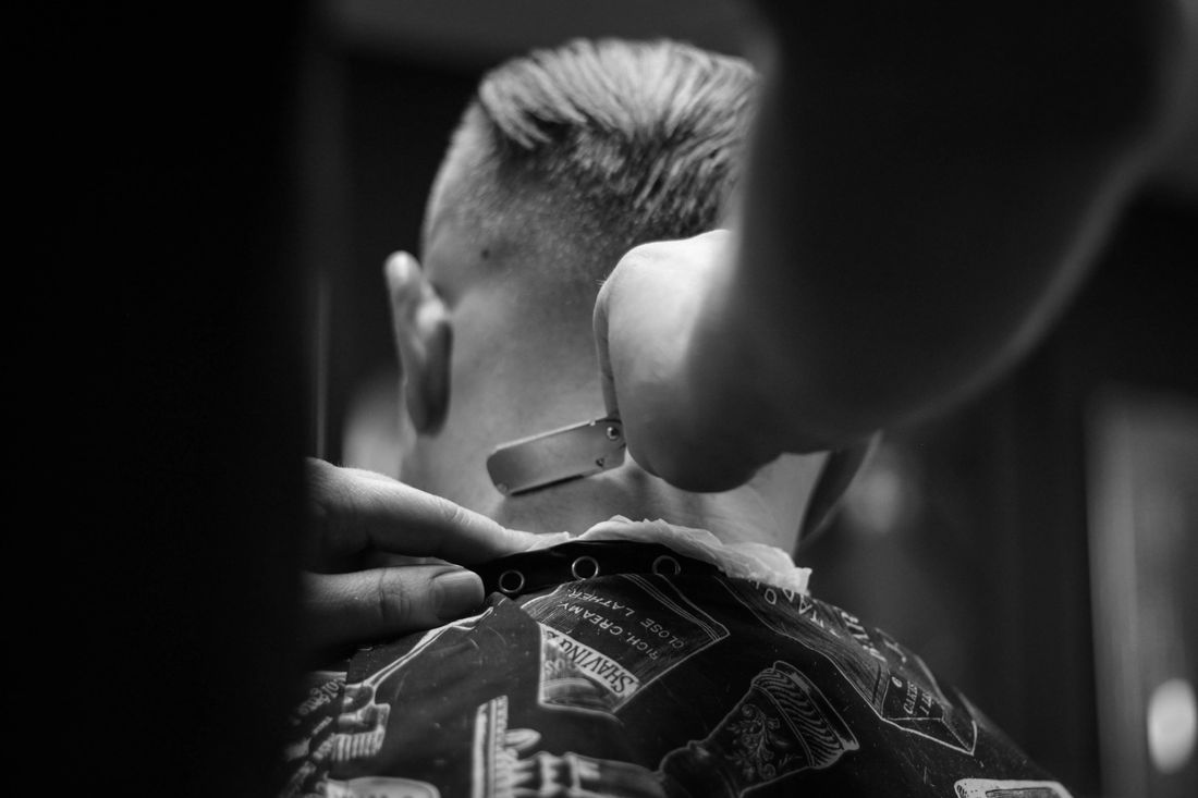 A barber fading the back of a client's head in a dark shop