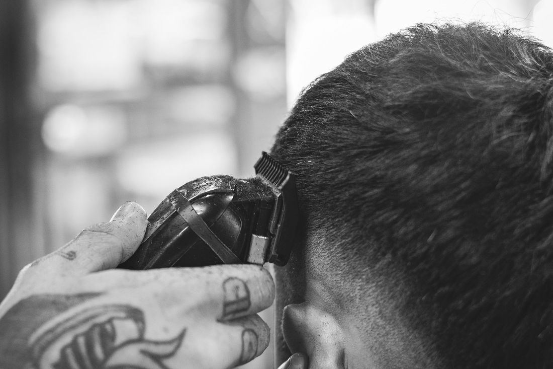 A tattooed barber running clippers up the back of a client's head