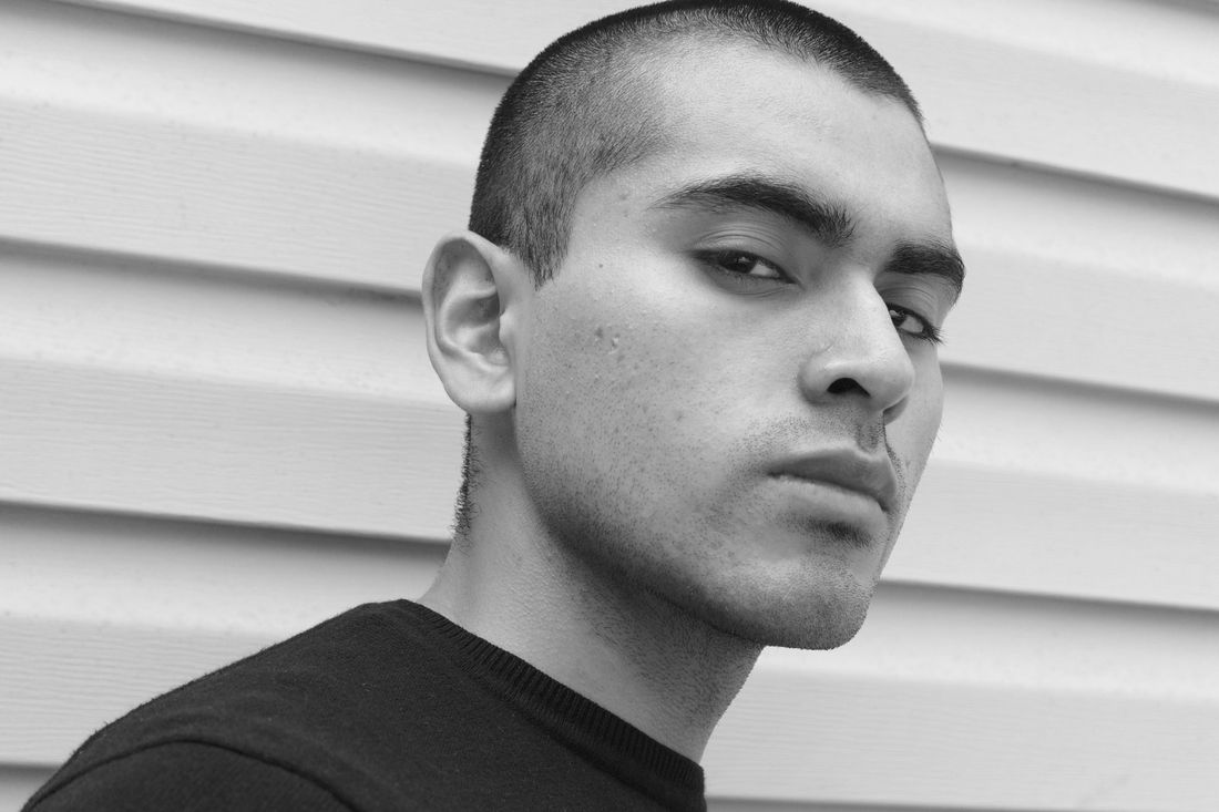 A young man with closely buzzed hair standing against siding