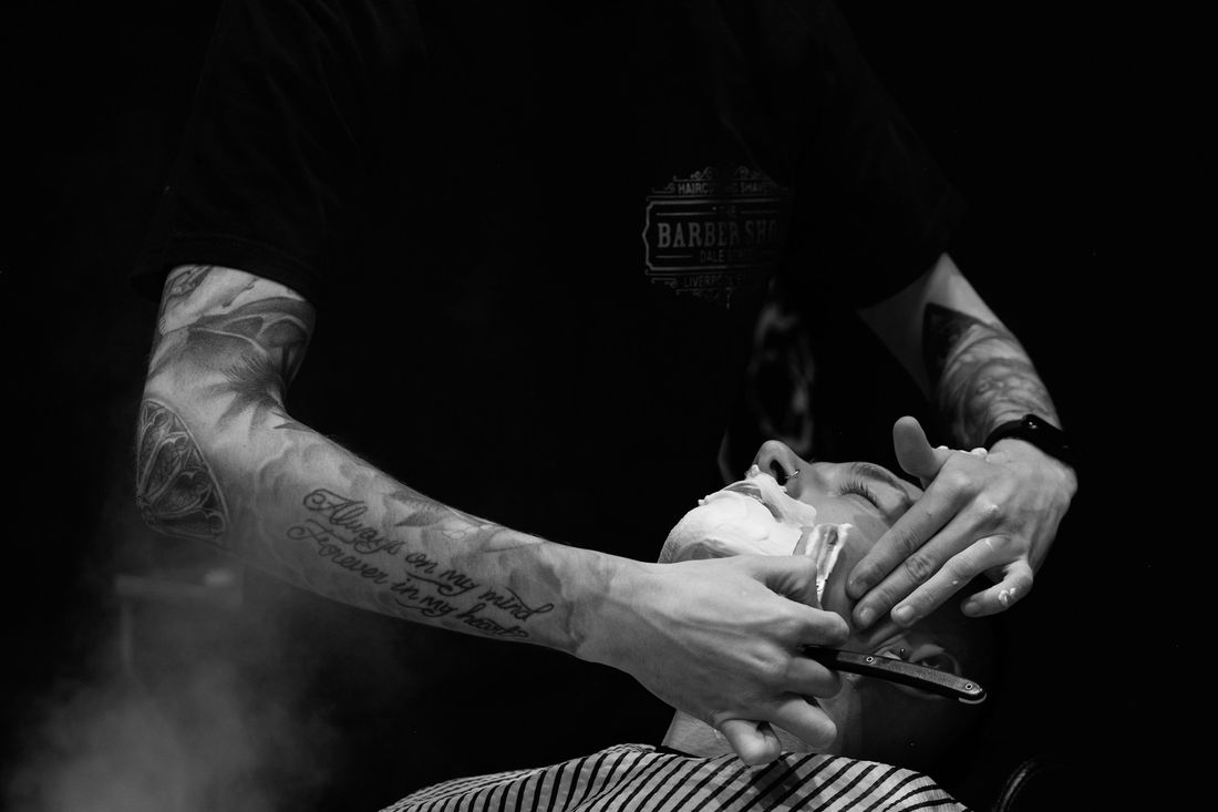 A barber working carefully on a client's face in a dimly lit shop