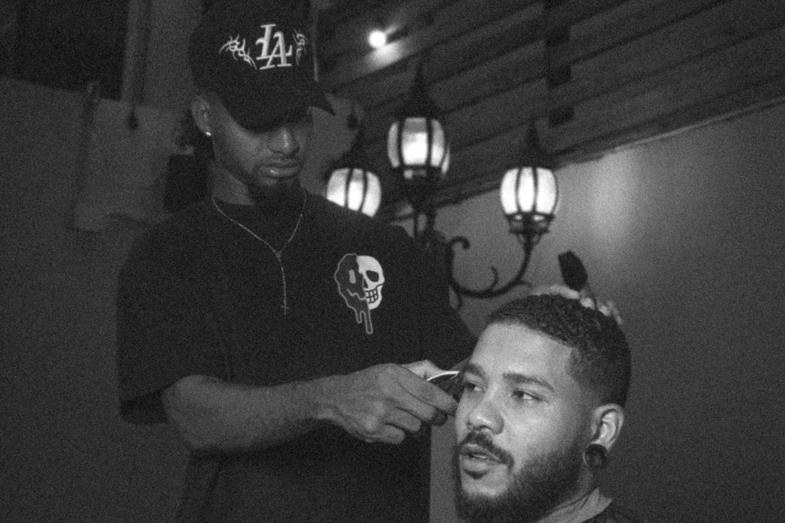A barber in a cap cutting a client's hair in a dimly lit shop