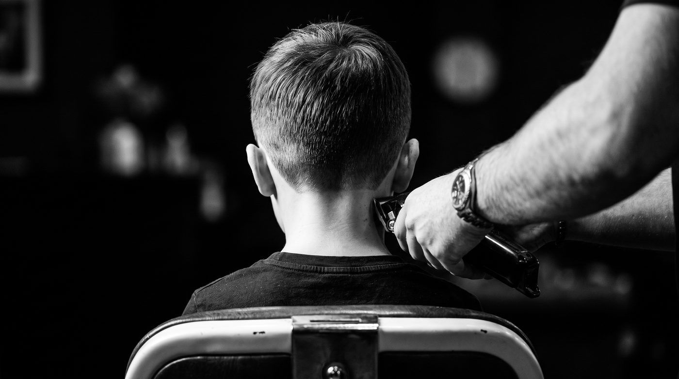 A barber&rsquo;s hand cleaning up the neckline at the back of a young boy&rsquo;s fresh haircut with clippers