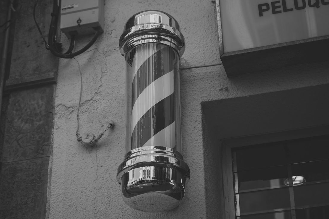 A traditional barber pole mounted on a gray wall beside a shop door