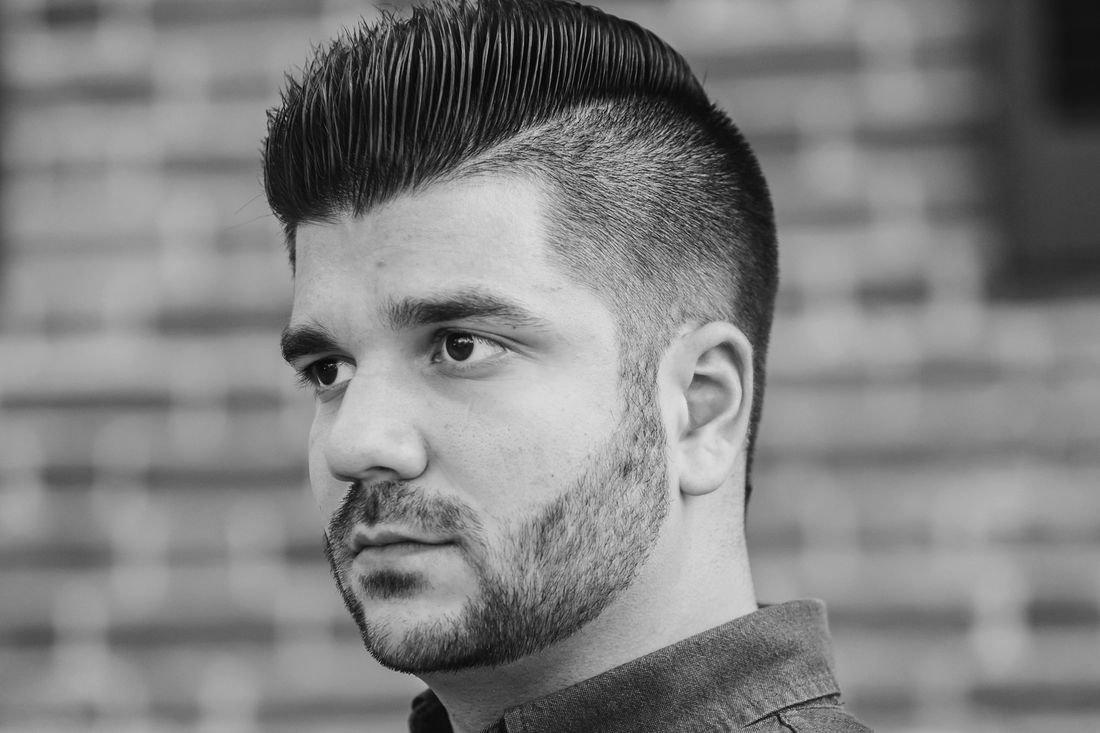A man with a short haircut and full trimmed beard looking out of frame