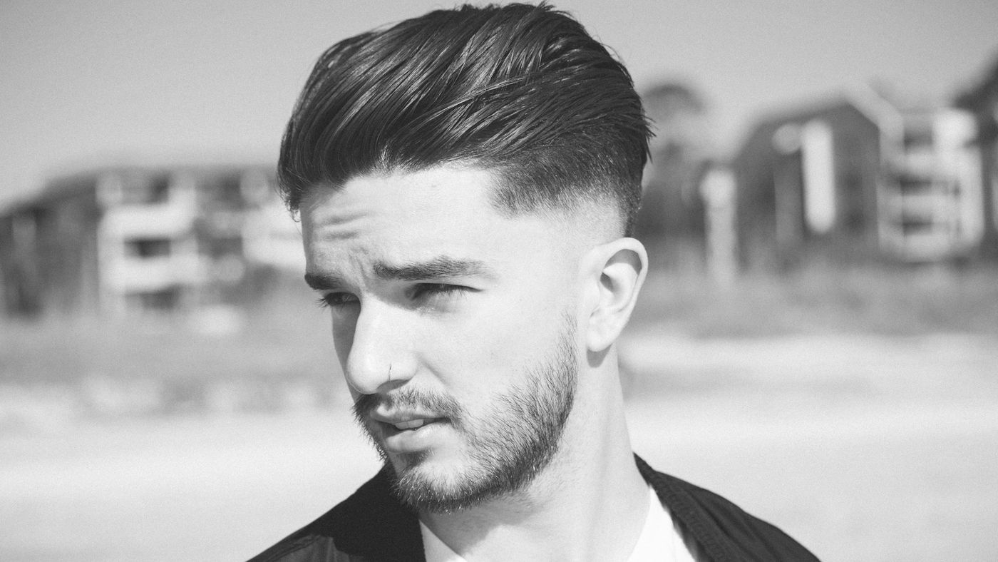 A man with a short textured haircut and a neat beard looking off to the side