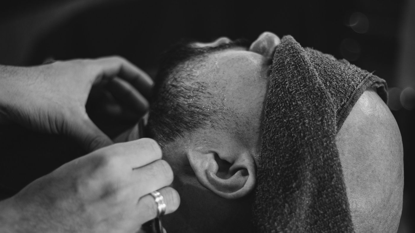 A barber cleaning up the neckline of a client with a towel around his shoulders
