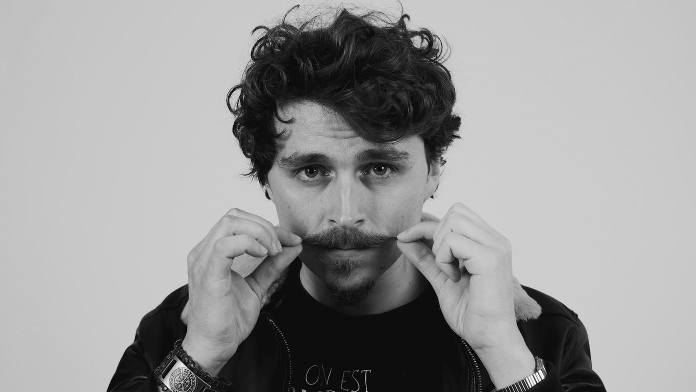 A curly-haired man twisting the ends of his mustache